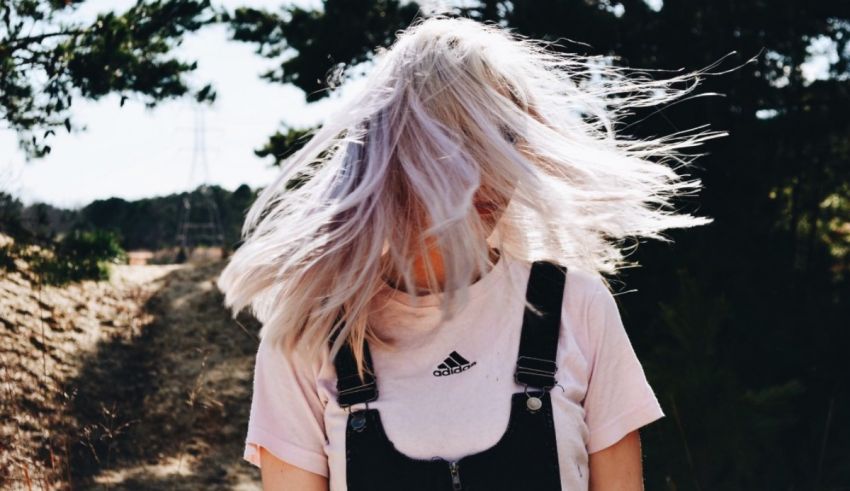 A girl wearing overalls and a pink shirt with her hair blowing in the wind.