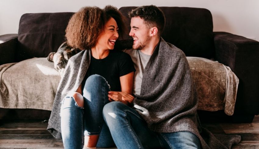 A couple sitting on a couch with a blanket wrapped around them.