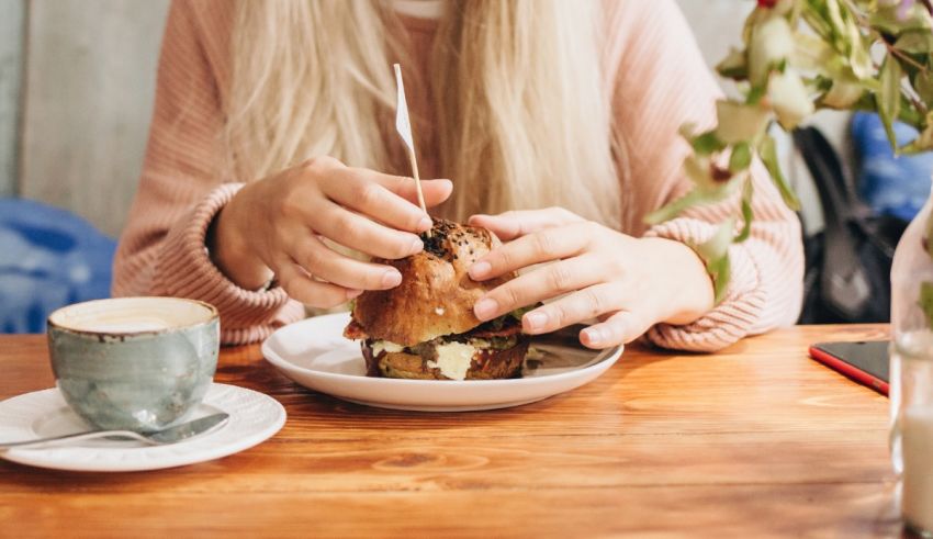 A woman eating a burger at a table with a cup of coffee.