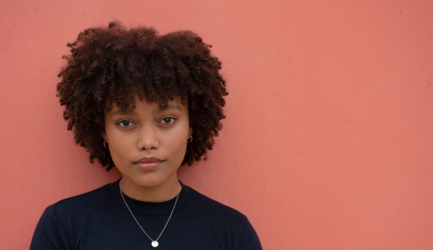 A young woman with afro hair standing against a pink wall.