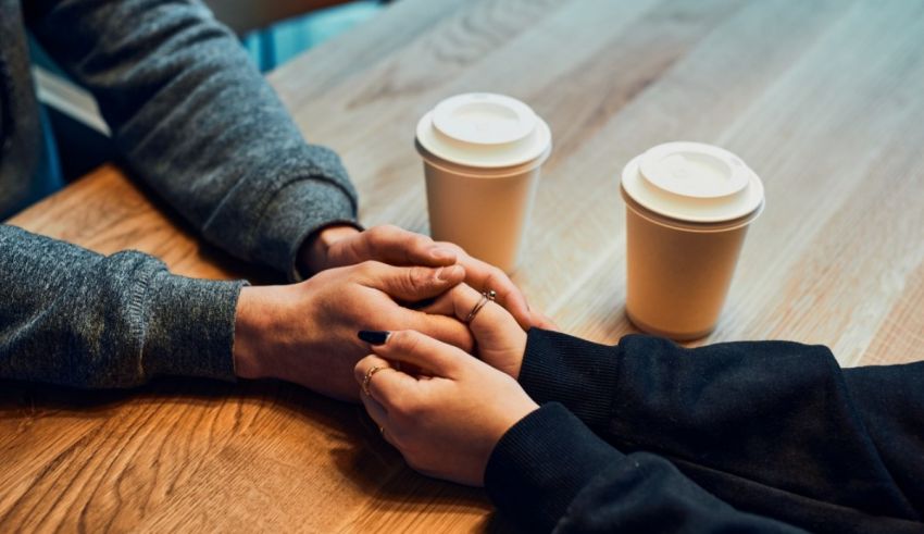 Two people holding hands at a table with coffee cups.