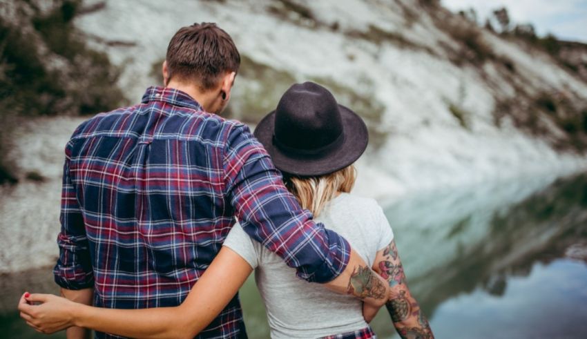 A couple with tattoos standing next to a river.