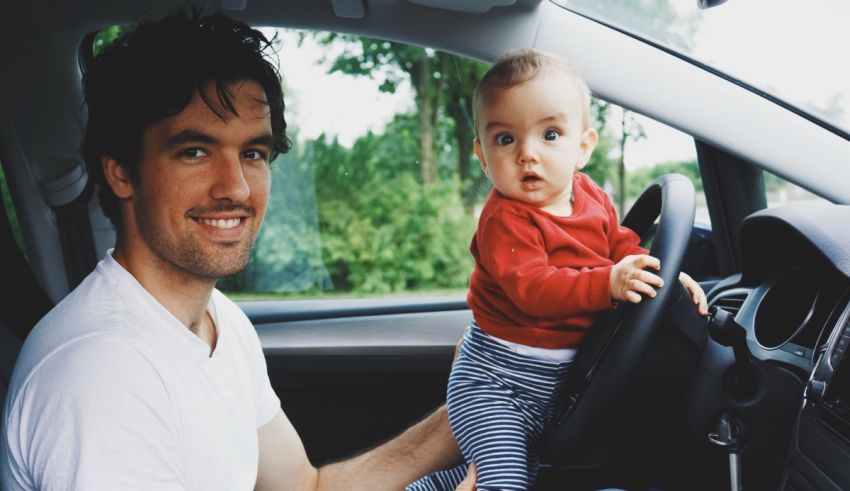 A man holding a baby while driving a car.