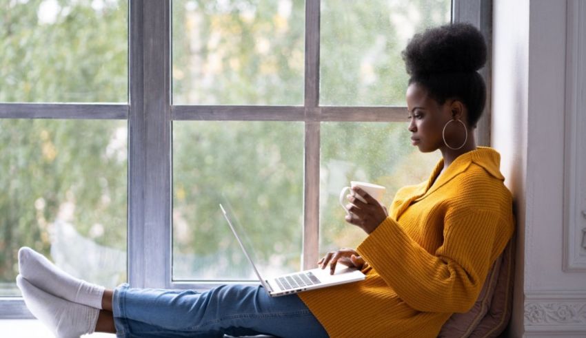 A woman is sitting on a window sill with a laptop.