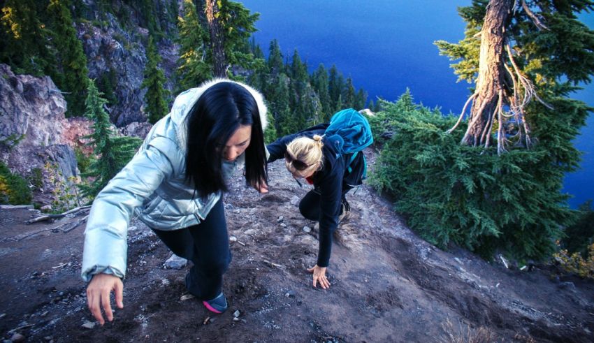 Two women hiking up a rocky mountain with a lake in the background.