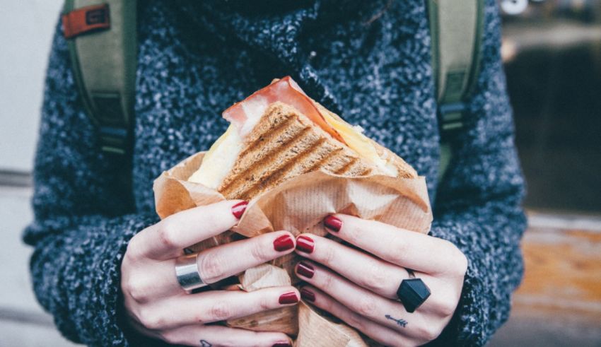 A woman holding a sandwich in a paper bag.