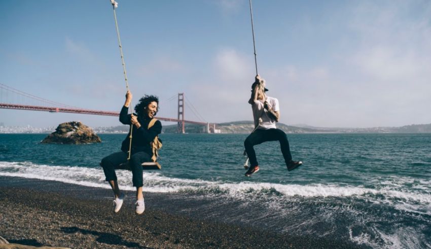 Two people swinging on a rope near the golden gate bridge.