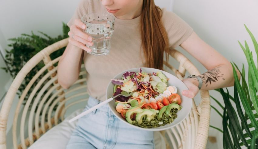 A woman is sitting in a wicker chair with a bowl of salad and a glass of water.