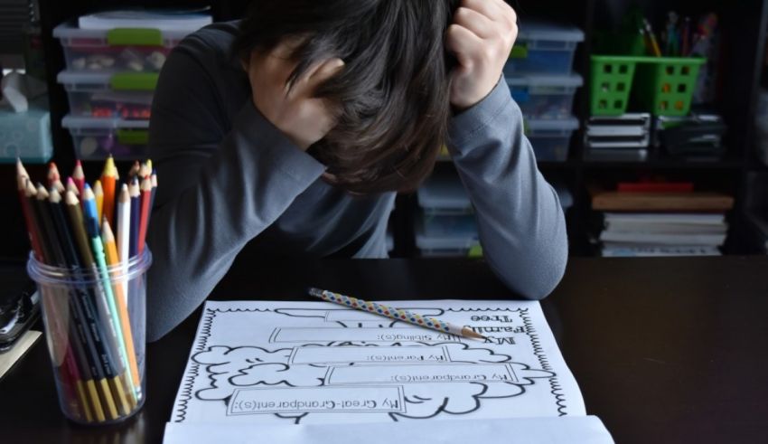 A child is sitting at a desk with a paper and pencils.