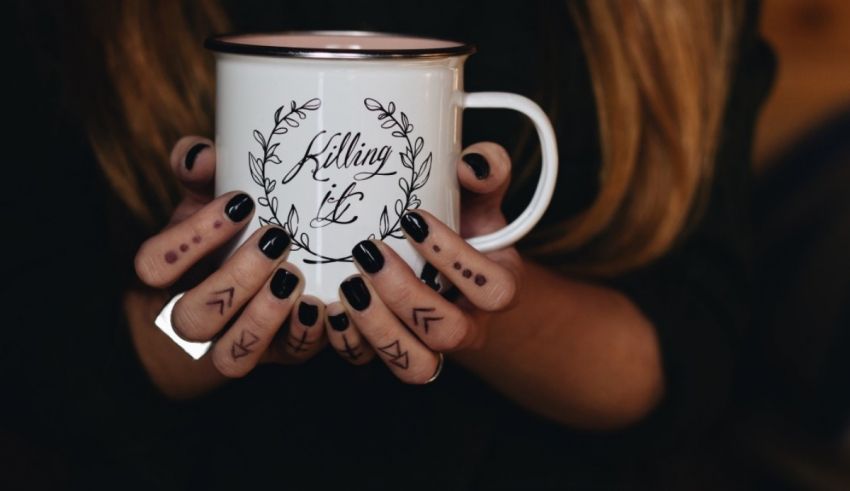 A woman holding up a mug with tattoos on it.