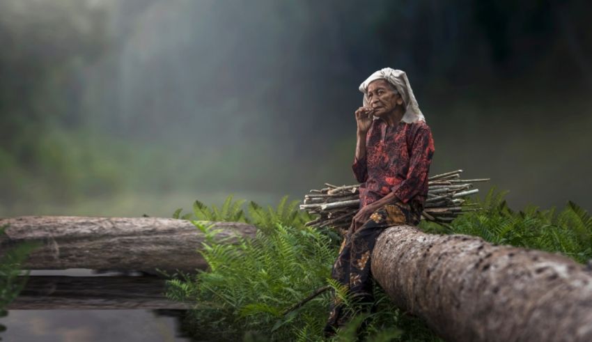 An old woman sitting on a log in the water.