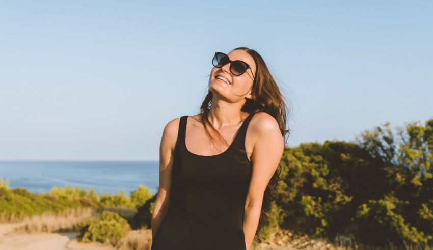 A woman wearing sunglasses and a black dress standing on a beach.