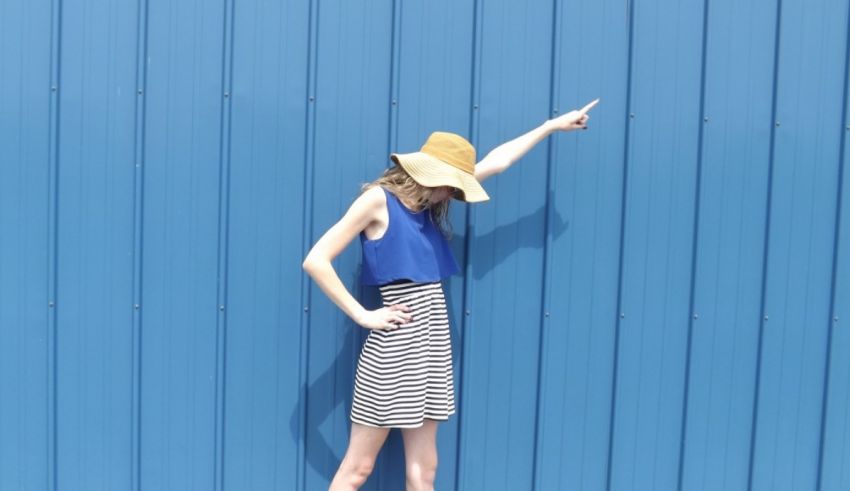 A woman in a striped dress leaning against a blue wall.