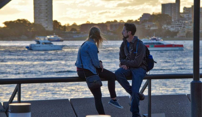 Two people sitting on a railing overlooking a body of water.