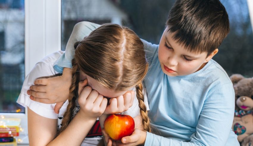 A boy and a girl holding an apple in front of a window.