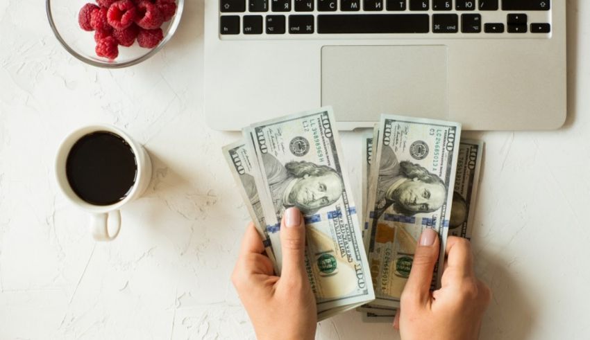 A woman's hands holding a stack of money next to a laptop.