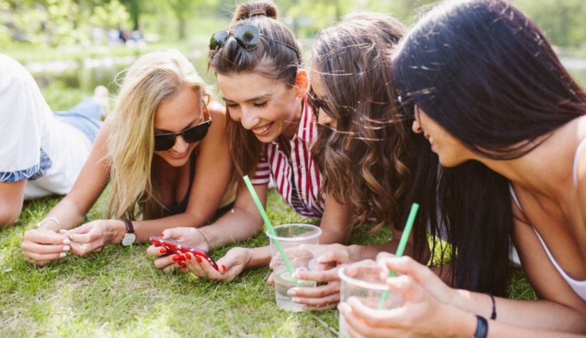 A group of friends laying on the grass looking at their cell phones.