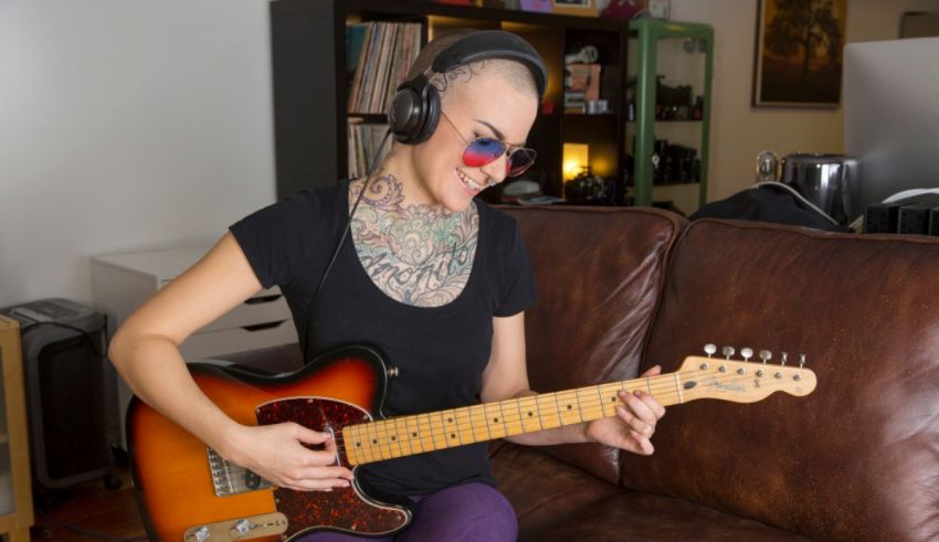 A woman with tattoos playing an electric guitar on a couch.