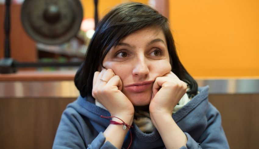 A woman is sitting in a cafe with her hands on her face.