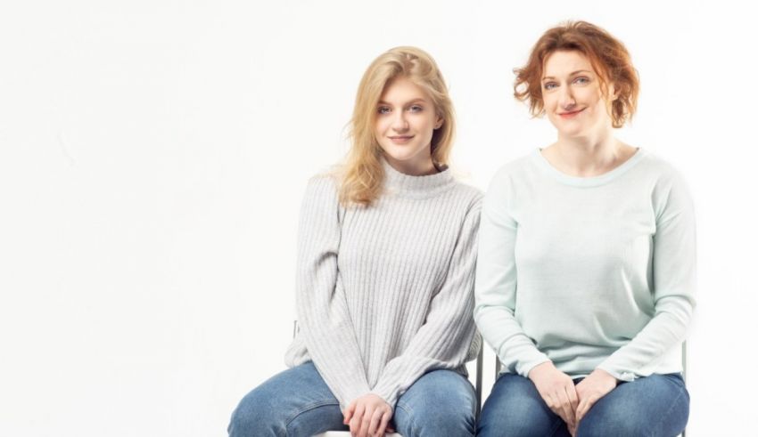 Two women sitting on a chair in front of a white background.