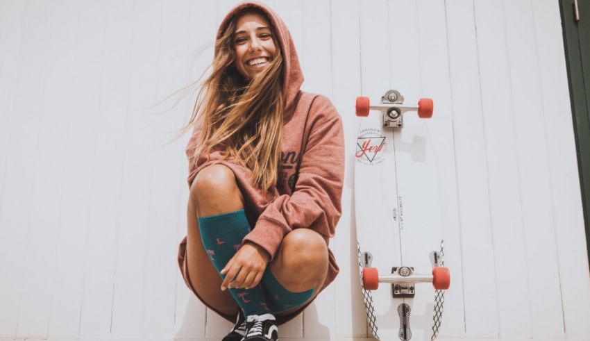 A girl in a hoodie sitting next to a skateboard.