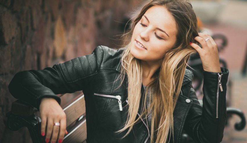 A young woman in a leather jacket leaning on a bench.