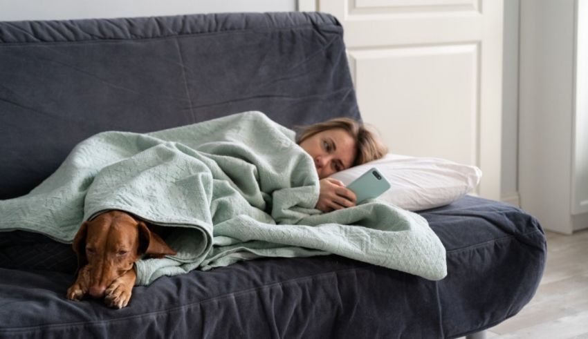 A woman is sleeping on a couch with her dog under a blanket.