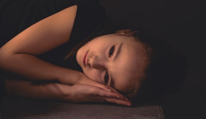 A little girl laying on a concrete floor with her hand on her head.