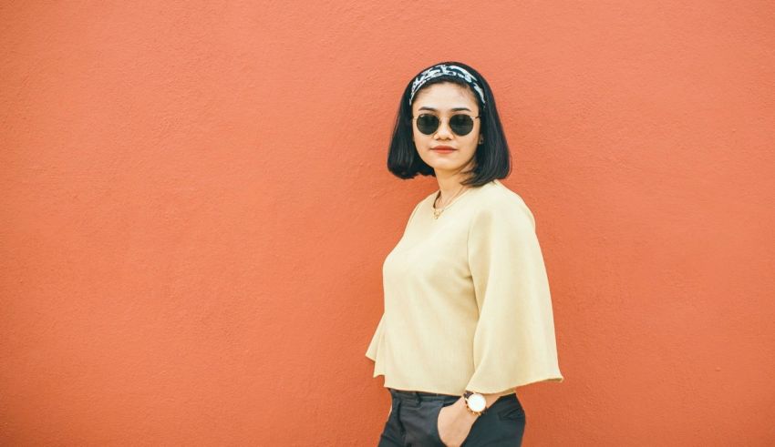 Asian woman in yellow top and black pants posing against an orange wall.