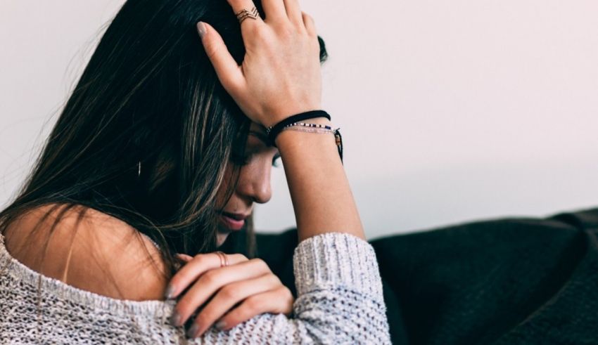 A woman is sitting on a couch with her hands on her head.