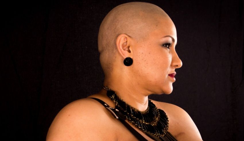 A woman with a shaved head looking at a black background.
