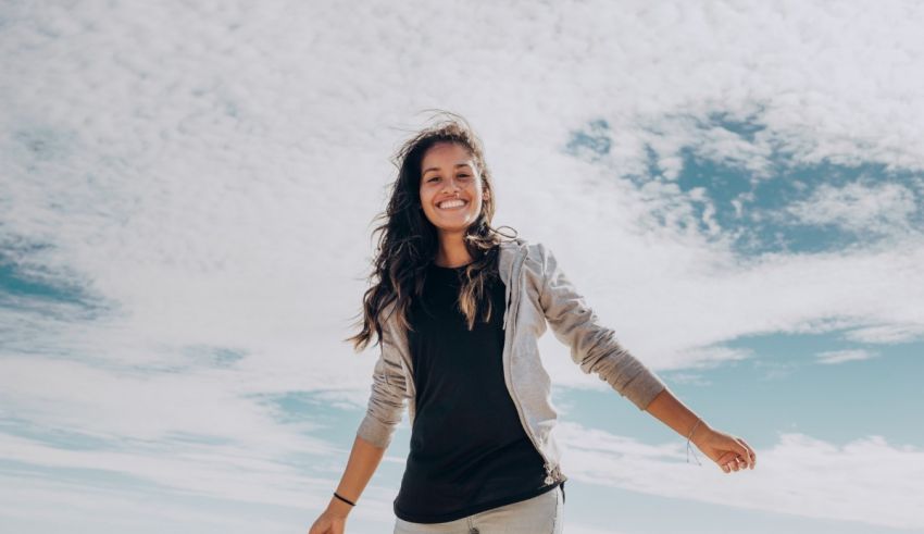 A young woman is standing on a beach with clouds in the background.