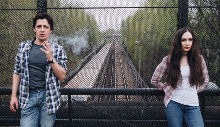 A young man and woman standing next to a train track.