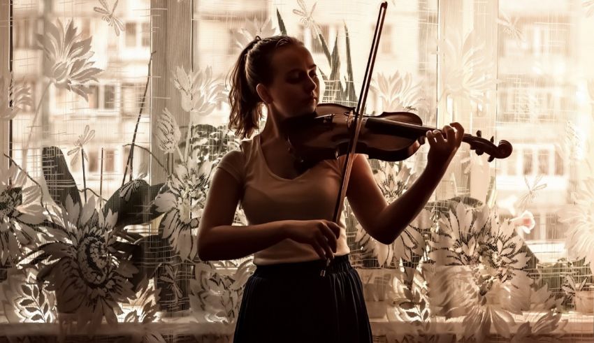 A girl playing the violin in front of a window.