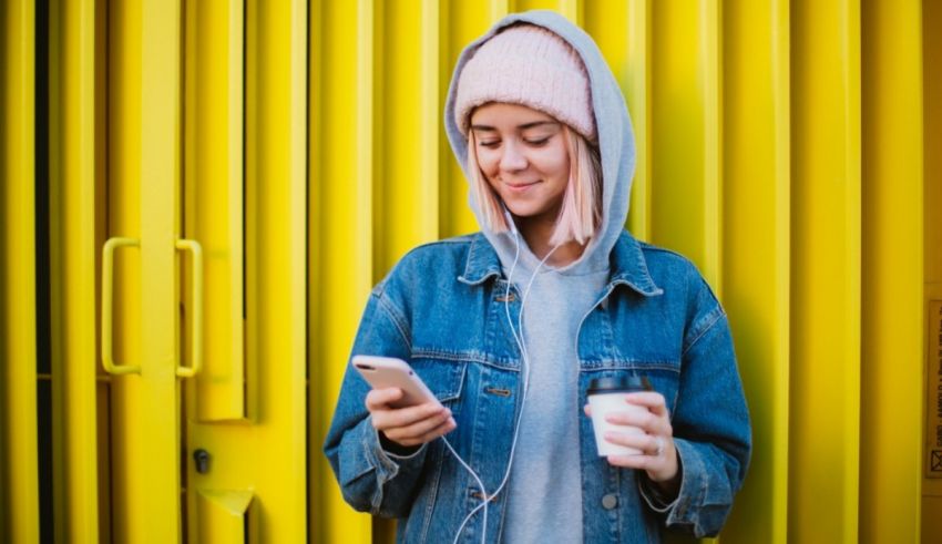 A girl is holding a cup of coffee while listening to music on her phone.