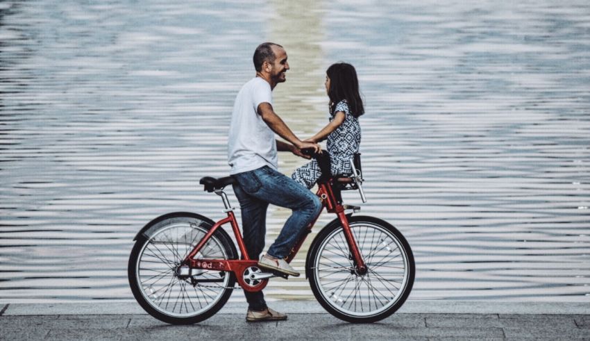 A man and a girl riding a bicycle near a body of water.