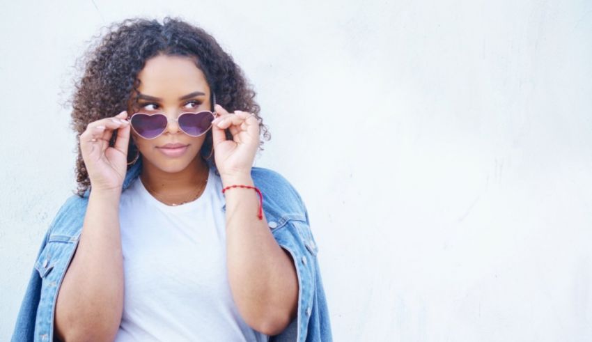 A woman with curly hair wearing sunglasses and a denim jacket.