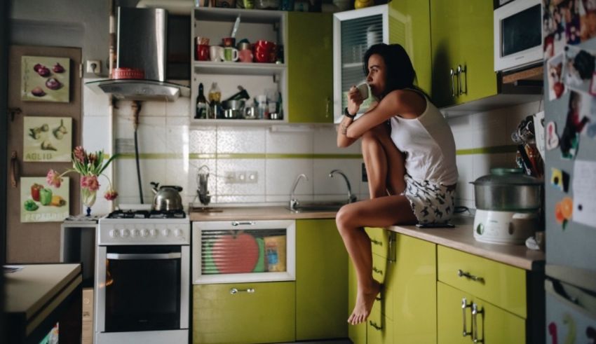 A woman sitting on top of a green cabinet in a kitchen.