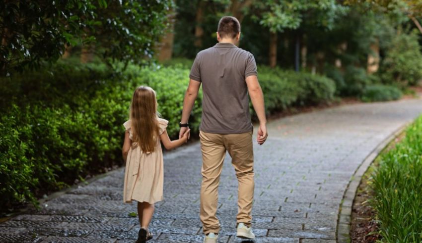 A father and daughter walking down a path in a park.
