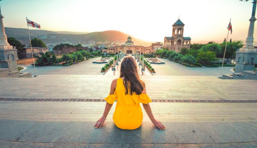 A woman in a yellow dress sits on the steps of a city.
