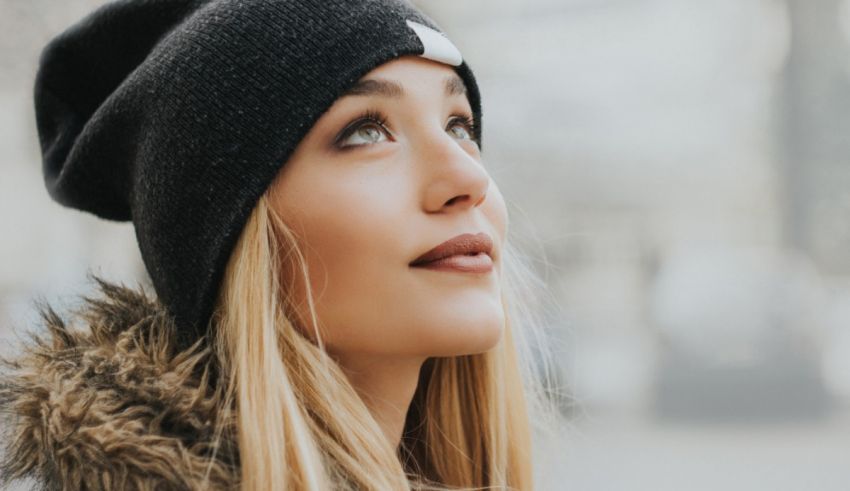 A young woman wearing a beanie looking up at the sky.