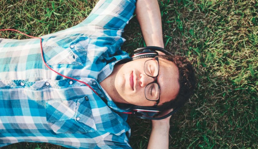 A young man laying on the grass listening to music.