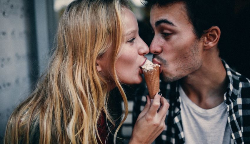 A man and woman kissing while eating an ice cream cone.