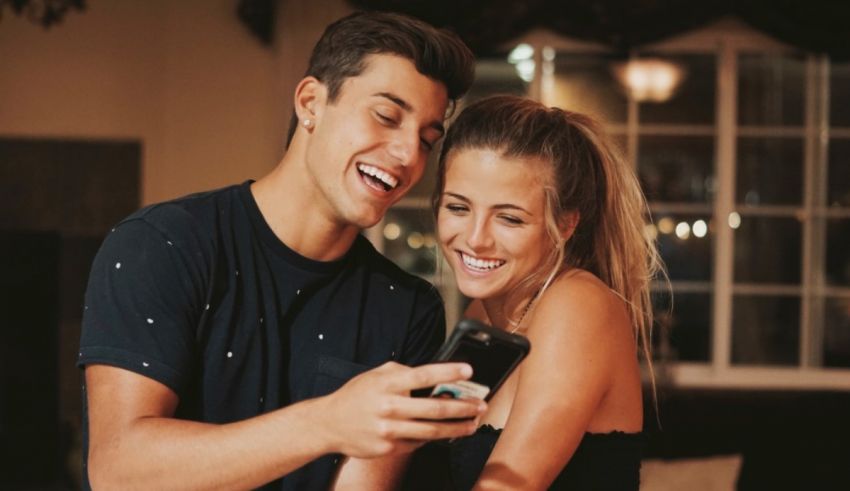 A man and woman are smiling while looking at a cell phone.