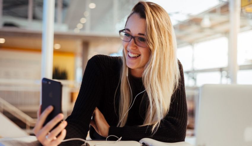 A woman is smiling while using her phone in an office.