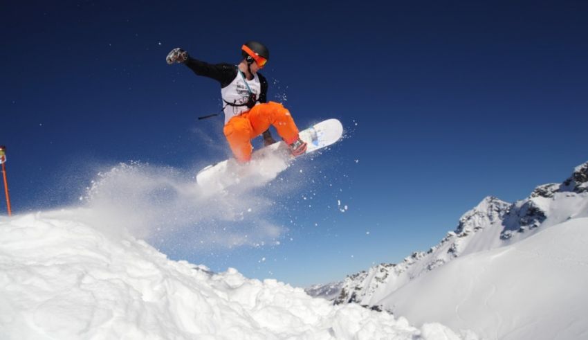 A snowboarder in the air over a snow covered mountain.