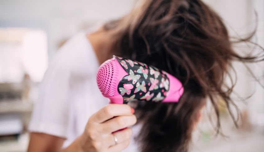 A woman is drying her hair with a pink hair dryer.