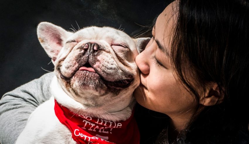 A woman kissing a french bulldog with a red bandana.