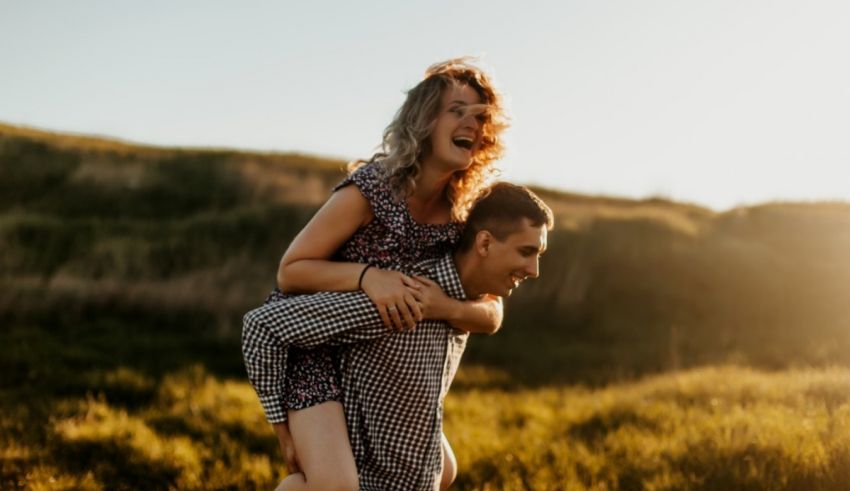 A man is piggybacking a woman in a field at sunset.