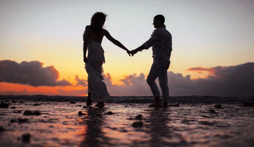 A bride and groom holding hands on the beach at sunset.